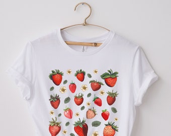 May include: White t-shirt with a red and green strawberry print. The strawberries are scattered across the shirt and have green leaves and white flowers.