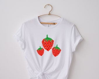 May include: White t-shirt with a graphic of three red strawberries with green leaves.