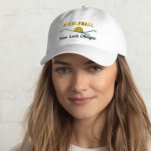 May include: White baseball cap with an embroidered design featuring a yellow pickleball, green mountains, and the text "Pickleball San Luis Obispo".