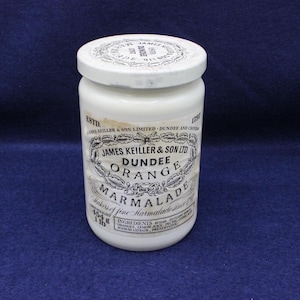 May include: A white ceramic jar of Dundee Orange Marmalade. The jar has a white lid and a label with text that reads "James Keiller & Son Ltd Dundee Orange Marmalade". The jar weighs 1 lb (454 g).