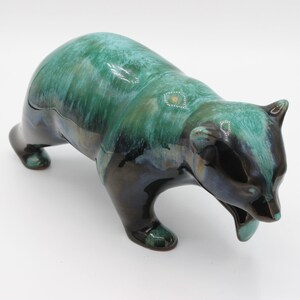 Pode incluir: Uma estatueta de urso em cerâmica com um esmalte brilhante que apresenta um gradiente de cor que transita do azul escuro e preto na base para um verde turquesa vibrante nas costas e na cabeça. O urso é retratado numa postura de caminhada.