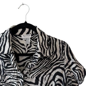 May include: A black and white zebra print blouse with short sleeves, hanging on a black hanger. The blouse has a collared neckline and a button-down front. The label reads "ALLISON TAYLOR PETITE".