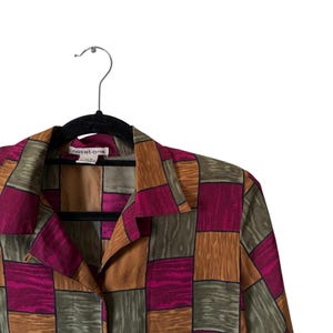 May include: A button-down shirt with a geometric pattern in shades of burgundy, brown, and olive green. The shirt is hanging on a black hanger. The brand name "notations" is visible on the label.