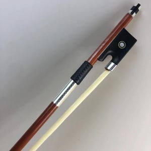 May include: A violin bow with a dark brown wooden shaft and a black frog. The bow has a silver winding and a light-colored horsehair. The frog has a white pearl inlay. The bow is angled diagonally.