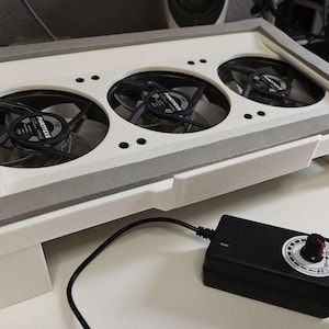 May include: White cooling pad with three black fans and a black power adapter with a speed control knob. The fans have the text "Arctic" printed on them.