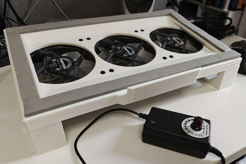 May include: White cooling pad with three black fans and a black power adapter with a speed control knob. The fans have the text "Arctic" printed on them.
