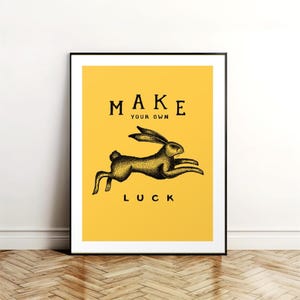 Könnte beinhalten: Ein gelber Poster mit schwarzem Text und einer Schwarzweißillustration eines laufenden Kaninchens. Der Text lautet "MAKE YOUR OWN LUCK".