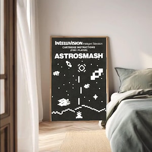 May include: A framed poster featuring the Intellivision game Astrosmash. The black background displays white pixelated graphics of stars and geometric shapes. The text reads "Intellivision Intelligent Television" and "Cartridge Instructions (For 1 Player)."