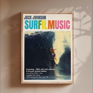 May include: A framed poster for a Jack Johnson Surf Music screening featuring a surfer riding a large wave. The text reads Jack Johnson Surf Music, Screening + Q&A with Jack Johnson & Director Emmett Malloy, June 22nd, 2026, 7pm, Angelika Film Center.