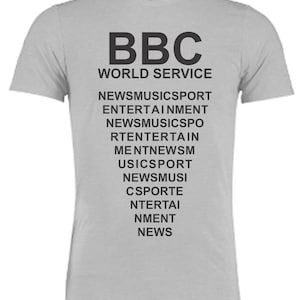Könnte beinhalten: Ein hellgraues Kurzarm-T-Shirt mit schwarzem Aufdruck, der BBC WORLD SERVICE liest, gefolgt von einem sich wiederholenden Muster der Wörter NEWS MUSIC SPORT ENTERTAINMENT, die in einer Dreiecksform auf der Vorderseite angeordnet sind.