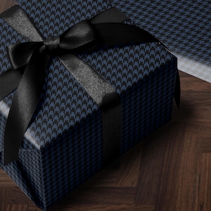 May include: A wrapped gift box with a black bow. The box is covered in blue and black houndstooth patterned paper. The bow and ribbon are black. The box is on a dark wood surface.