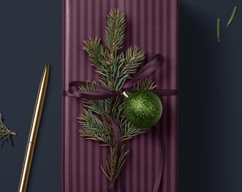 May include: A burgundy striped gift box with a green Christmas bauble and a sprig of pine needles tied with a burgundy ribbon.
