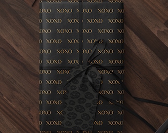 May include: A black gift box with a gold XOXO pattern and a black and white lip print gift tag. The box is tied with a black ribbon and is sitting on a wooden surface.