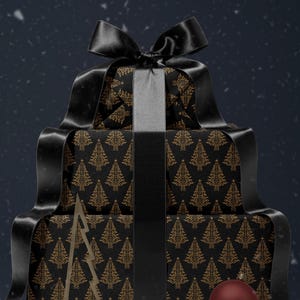 K&ouml;nnte beinhalten: Drei schwarze Geschenkboxen, die &uuml;bereinander gestapelt sind und in schwarzes Papier mit einem goldenen Weihnachtsbaum-Muster eingewickelt sind. Die oberste Box hat ein schwarzes Satinband, das zu einer Schleife gebunden ist. Ein goldener Weihnachtsbaum-Anh&auml;nger aus Metall befindet sich vor den Boxen, und ein roter Anh&auml;nger befindet sich auf der untersten Box.