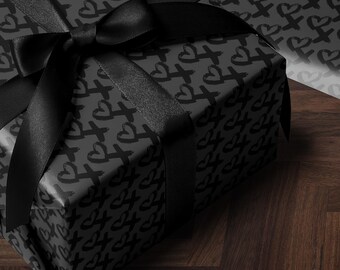 May include: A black gift box with a black ribbon is wrapped in black and white wrapping paper with a repeating pattern of hearts and crosses. The box is sitting on a dark wood surface.