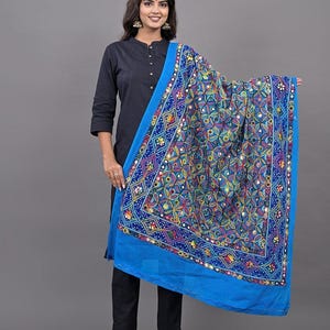 Könnte beinhalten: Ein leuchtend blauer Dupatta mit komplexer, mehrfarbiger Blumenstickerei und kleinen runden Spiegeln. Der Stoff hat einen breiten, einfarbigen blauen Rand und ein dichtes Muster aus ineinandergreifenden Formen mit leuchtenden Garnen.