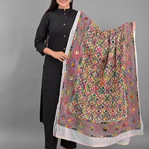 Könnte beinhalten: Eine schwarze langärmelige Tunika mit passender Hose, kombiniert mit einem großen, rechteckigen weißen Dupatta, das ein komplexes, mehrfarbiges Blumenmuster, geometrische Stickereien und kleine runde Spiegel im gesamten Stoff aufweist.