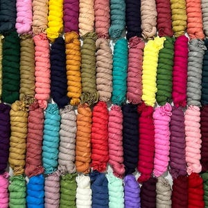 Puede incluir: Una colección de numerosas bufandas de tela largas, delgadas y enrolladas dispuestas en un patrón de cuadrícula. Las bufandas presentan una gran variedad de colores sólidos, incluyendo tonos de azul, rosa, amarillo, verde, rojo, morado, naranja, marrón, gris y negro.