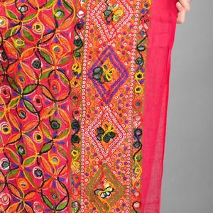 May include: A vibrant pink and orange textile featuring intricate embroidery with circular mirror accents. The fabric displays a repeating pattern of stitched floral motifs and geometric diamond shapes, finished with a solid pink border edge.