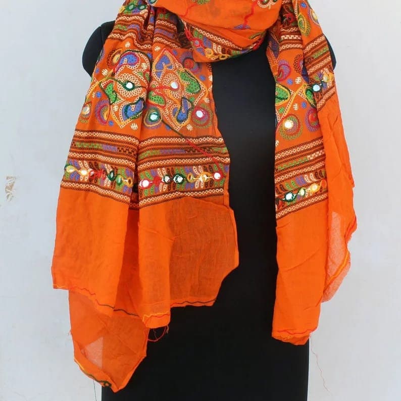 K&ouml;nnte beinhalten: Orangefarbener Schal aus Baumwolle mit bunten Stickereien und Spiegelverzierungen. Der Schal hat ein geometrisches Muster und ist mit floralen Motiven verziert.