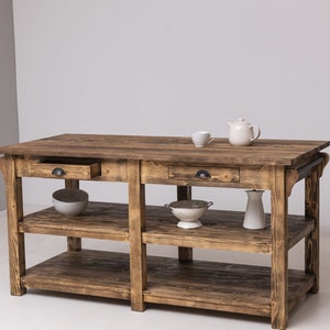 Könnte beinhalten: Eine rustikale Kücheninsel aus Holz mit zwei Schubladen und zwei Regalen. Die Insel ist aus recyceltem Holz gefertigt und hat eine natürliche Oberfläche. Sie verfügt über schwarze Metallschubladengriffe und einen Metallstangenhandgriff an der Seite.
