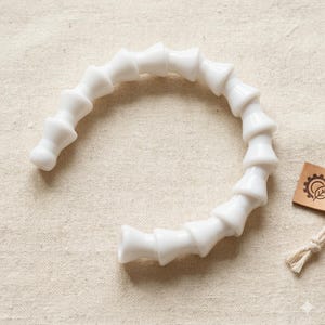 May include: A white, articulated plastic arm, resembling a segmented tube, is arranged in a semi-circle. The arm is composed of cone-shaped segments connected by ball joints. A small tag with a logo and a string are in the background.