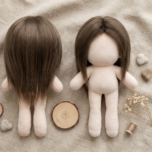 May include: Two blank fabric dolls with brown hair wigs. The dolls have a light beige body and are standing upright. One doll is facing forward, and the other is facing backward. A wooden slice with a leaf design is in front of one doll.
