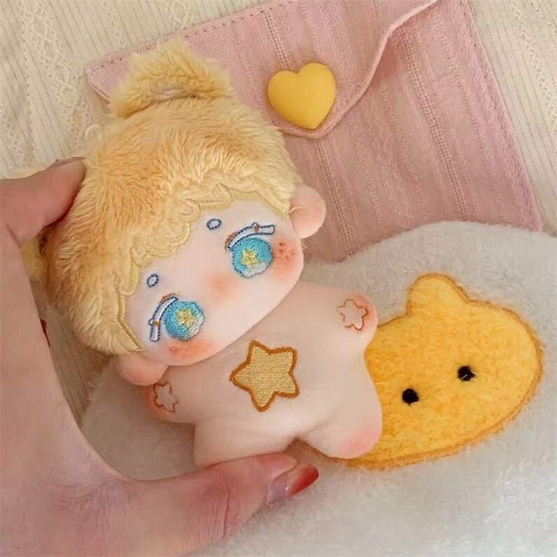May include: A small plush toy with blonde hair, blue eyes, and a star design on its chest. The toy is holding a yellow plush cloud with black eyes.