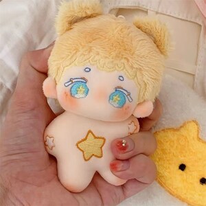 May include: A plush toy with a yellow head and a pink body. The toy has embroidered eyes, a blue and white headband, and a yellow star on its chest.