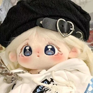 May include: A plush doll with large blue eyes, wearing a black beret with a heart-shaped buckle and a white hoodie with black text.