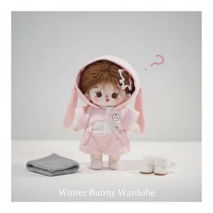 May include: A doll dressed in a pink bunny-eared hoodie, shorts, and a white top. The doll has brown hair and is accessorized with a grey knitted scarf and white boots. The text "Winter Bunny Wardobe" is at the bottom.