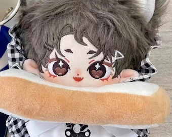 May include: A plush doll with a wolf-like appearance, featuring gray fur, large expressive eyes, and a small red mouth. The doll is wearing a white outfit with a black and white checkered hood and holding a plush hot dog.
