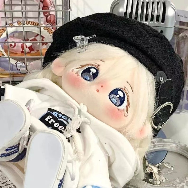 May include: A white plush doll with large blue eyes and rosy cheeks, wearing a white hoodie with the word "free" printed on it, a black beret, and white shoes.