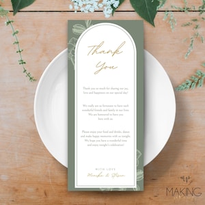 Może przedstawiać: Karta z podziękowaniami ślubnymi z szałwiowym zielonym tłem i białym łukiem. Słowa "Thank You" są w złotym skrypcie. Karta zawiera wiadomość z podziękowaniami i jest umieszczona na białym talerzu.