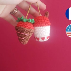 Peut inclure: Deux ornements faits à la main au crochet : une fraise enrobée de chocolat et un bubble tea. La fraise a un dessus rouge, des feuilles vertes et une base marron avec des spirales roses. Le bubble tea est rouge et blanc avec des cœurs.