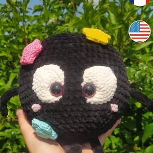 May include: Black crocheted plush toy with large eyes, a pink nose, and colorful star-shaped accents. The toy has small arms and legs.