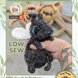 May include: A dark gray crocheted fly plush toy with large blue glittery eyes and white wings. The image includes text reading FUNGUS THE FLY, LOW SEW, and PDF Crochet Pattern designed and written by Jessica Morgan of Mo2 Designs.