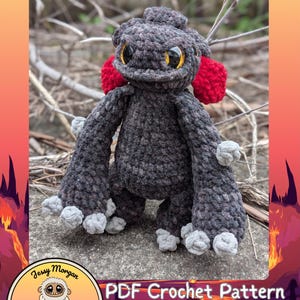 May include: A handmade crochet toy of Vexley the Voidscale, a dragon-like creature with a dark grey body, red ear tufts, and large yellow eyes. The image includes text that reads "VEXLEY THE VOIDSCALE" and "PDF Crochet Pattern".