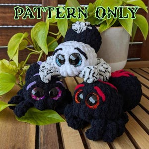 Puede incluir: Tres juguetes de araña amigurumi de crochet. Uno es negro con detalles rojos, otro es negro con detalles morados y el último es blanco con detalles negros. Los tres tienen grandes ojos saltones.