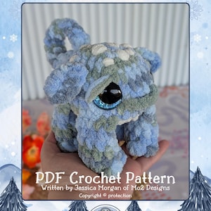 May include: A soft, blue and green crocheted toy, "Snorbo the Chubblump", with large eyes. The image includes the text "PDF Crochet Pattern" and the Mo2 Designs logo. The toy is held in a hand. The background is a winter scene.