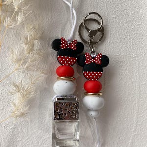 May include: Two keychains with a Minnie Mouse design. Each has a black and red polka dot bow, red and white beads, and a small perfume bottle. One keychain has a silver keyring.