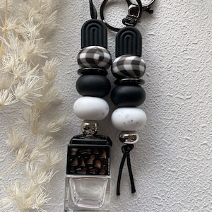 May include: Black and white checked beads with black and white marble beads, a black and brown diffuser, and a silver key chain. The beads are strung on a black cord with a black tassel.