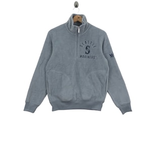 May include: A gray fleece pullover sweatshirt with a navy blue Seattle Mariners logo on the front and the word "Mariners" underneath. The sweatshirt has a half-zip closure.