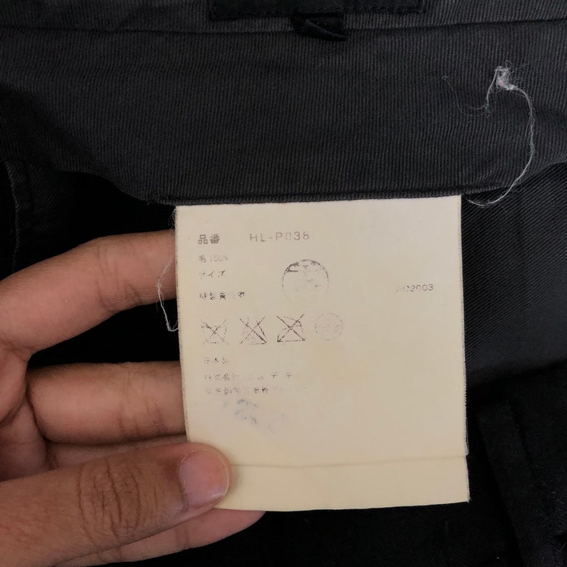 May include: Close-up of a clothing tag with Japanese text and the code "HL-P036". The tag is attached to black fabric. The tag also has several symbols and a date.