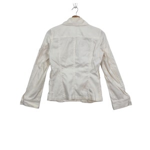 May include: A white, long-sleeved jacket with a button-up front and a collar. The jacket has a fitted silhouette and is made of a lightweight fabric.