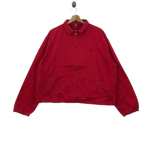 Puede incluir: Una chaqueta roja con cremallera y un pequeño logotipo bordado en el pecho izquierdo.