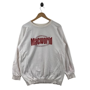 May include: Cream-coloured sweatshirt with the red text "Macworld" across the chest. The text is arched and has a smaller line of text above and below it. The sweatshirt is hanging on a wooden hanger.