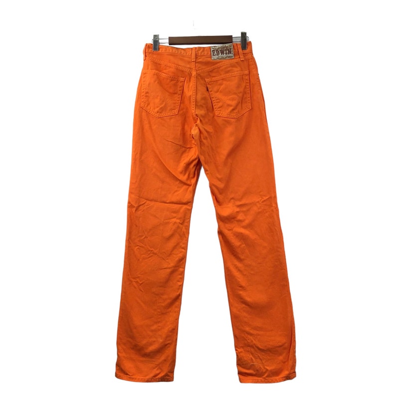Op de afbeelding: Een paar oranje rechte jeans met een bruin leren patch waarop "EDWIN" staat.