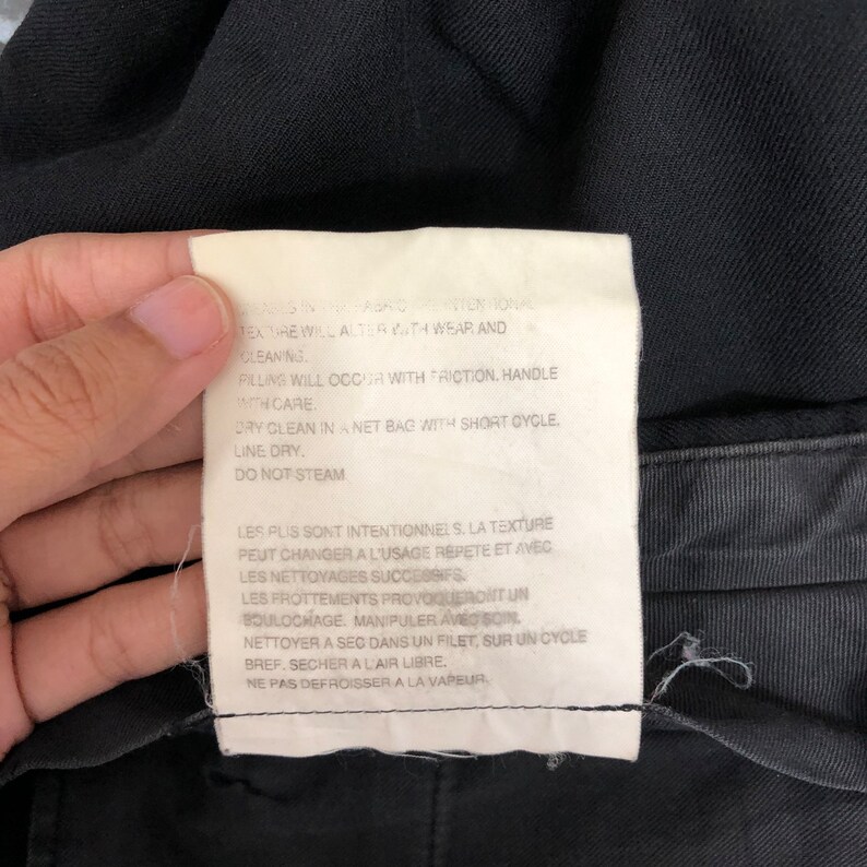 May include: A close-up of a white clothing tag with black text. The tag is attached to a black garment. The text includes washing instructions and care details. The tag also has French text.