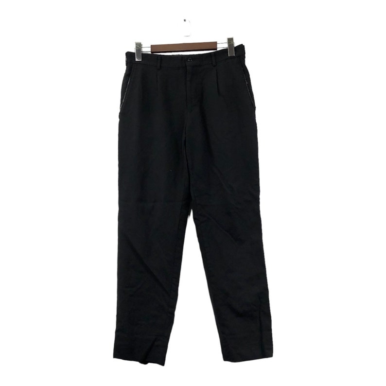 May include: Black trousers hanging on a wooden hanger. The pants have a button closure, belt loops, and pockets. The fabric appears to be a medium-weight material. The trousers are a solid black color.